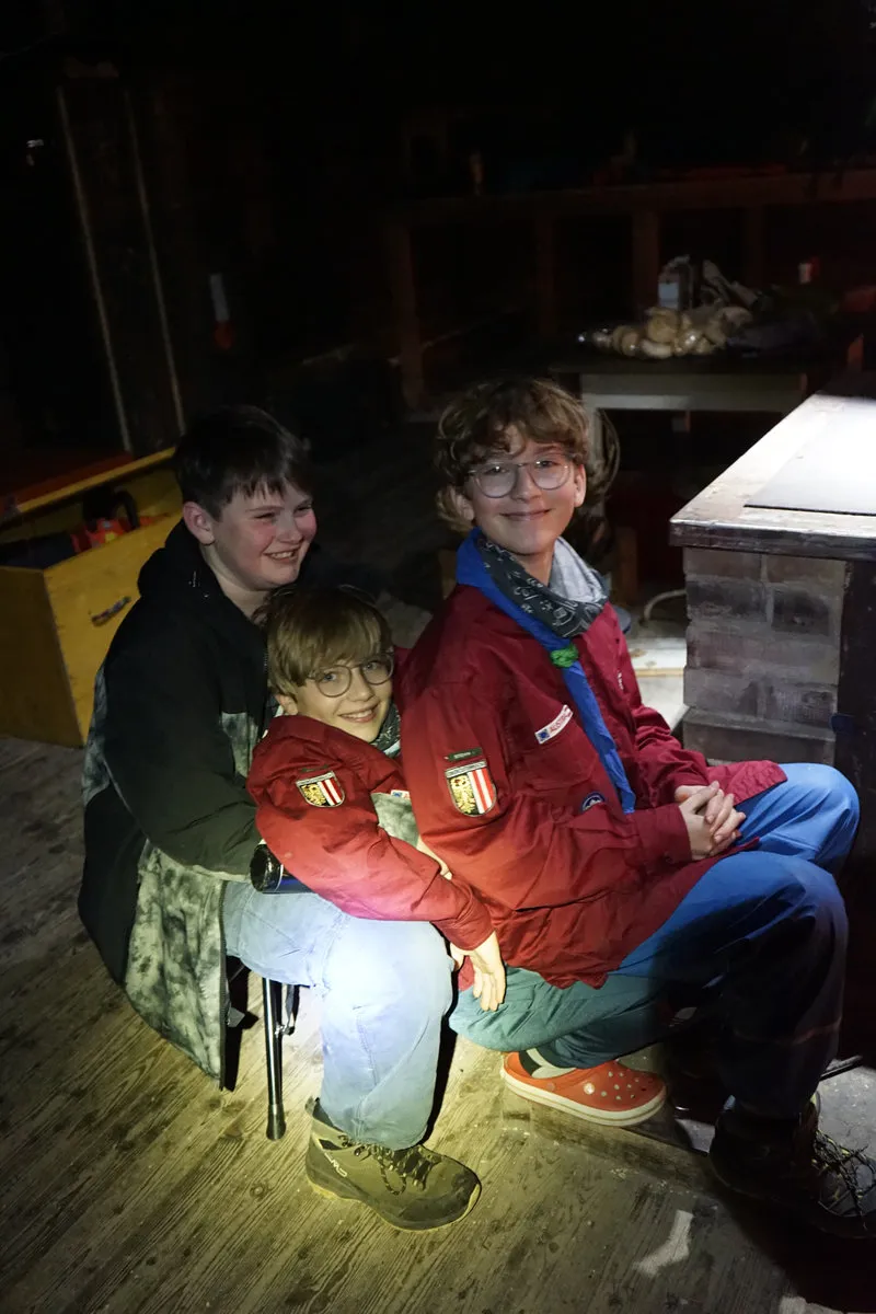 Drei Späher sitzen abends im Licht einer Taschenlampe in der Hütte