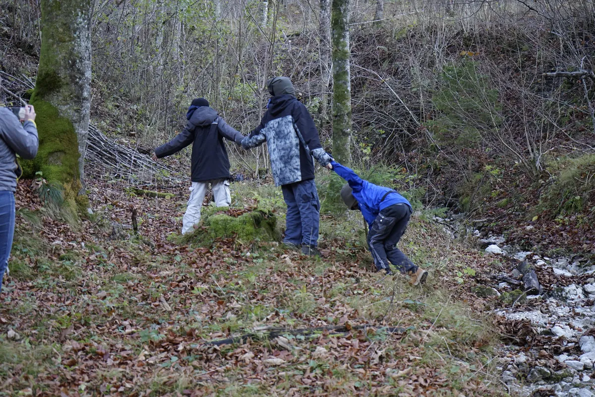 Späher halten sich an den Händen und balancieren über einen Waldhang am Bach