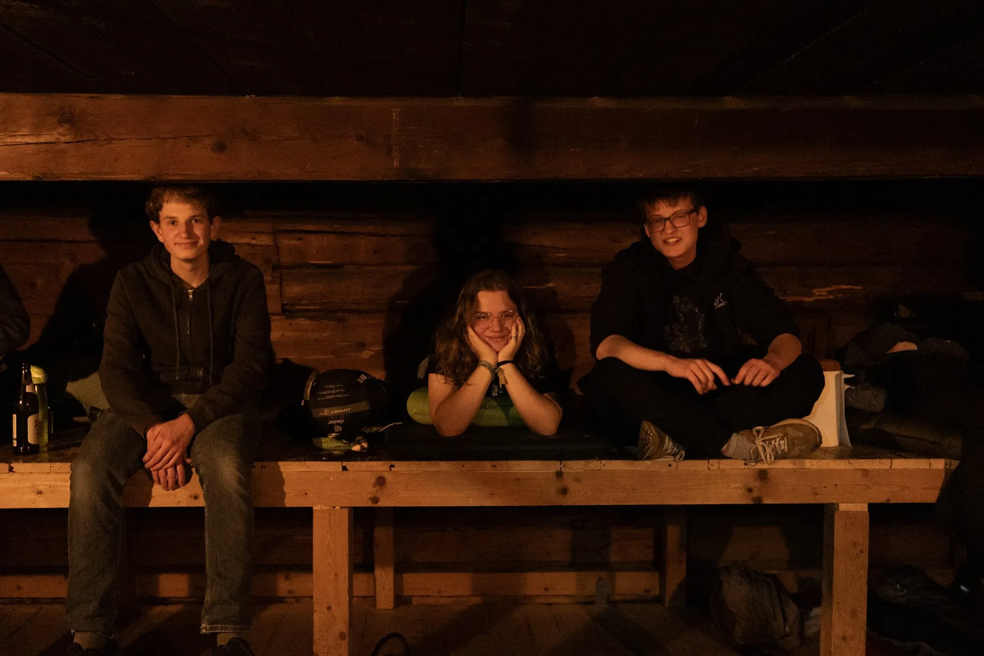 Drei RaRo sitzen am Abend auf dem Matratzenlager der Hütte und lächeln in die Kamera.