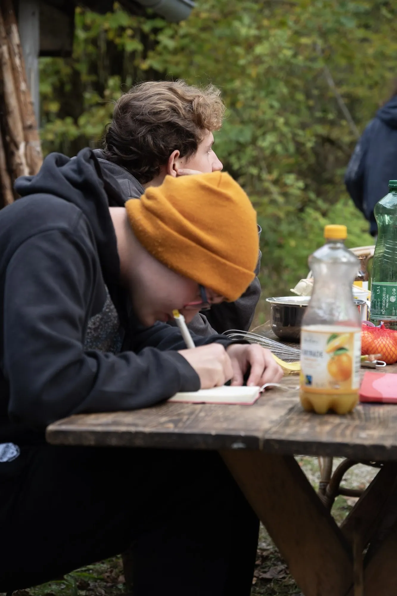 Ein RaRo mit orangefarbener Haube schreibt am Holztisch in ein Notizbuch.